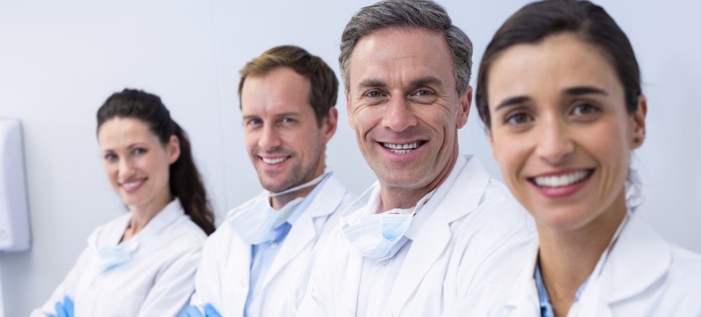 Four smiling dentists in white lab coats