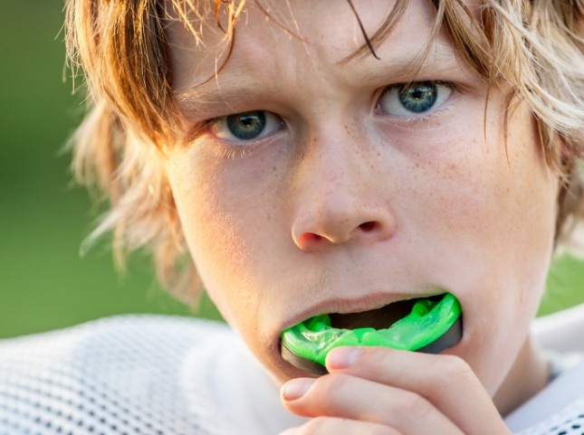 Young boy placing green athletic mouthguard over his teeth