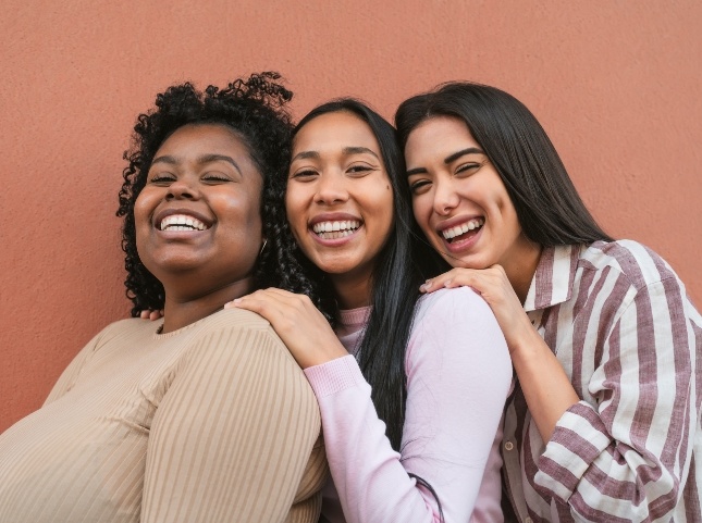Three women smiling together against orange wall