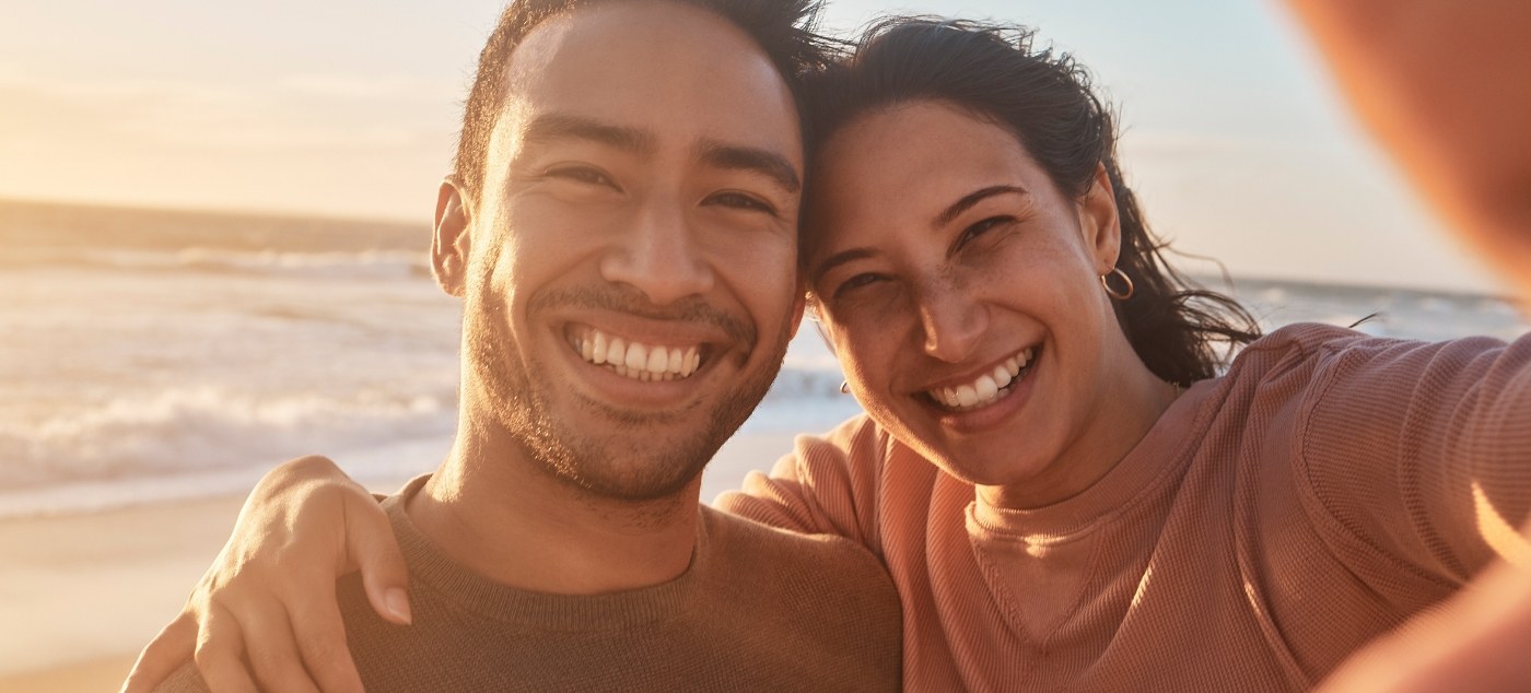 Man and woman taking selfie on beach after restorative dentistry in Dublin
