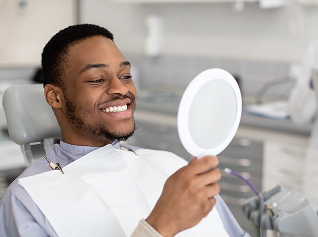Man smiling at reflection in handheld mirror