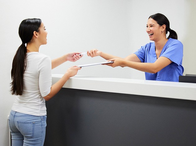 Smiling dental assistant handing patient form