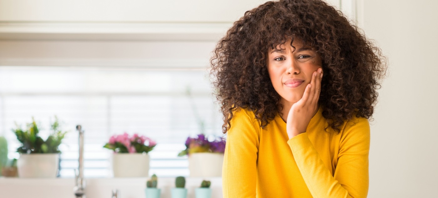 Woman in yellow seater wincing and holding her cheek