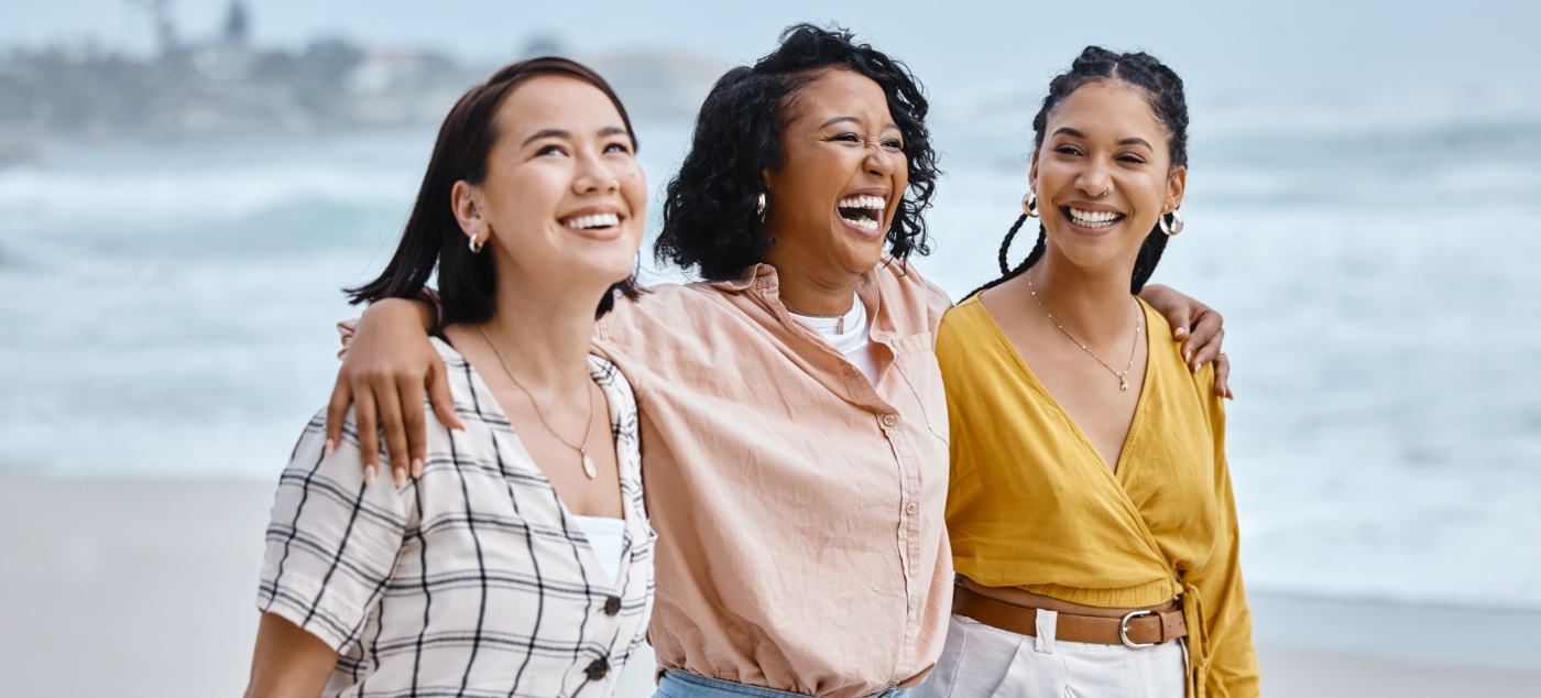 Three woman walking on beach with their arms around each others shoulders