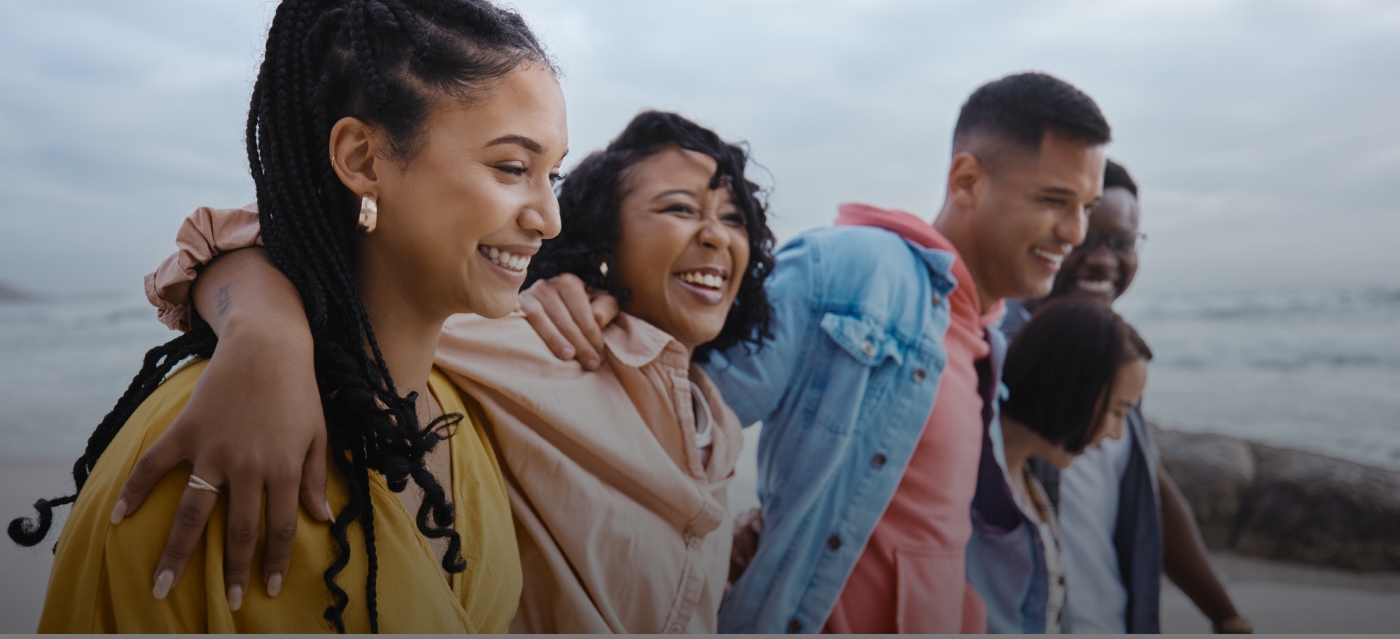 Five young adults laughing on beach with their arms around each other