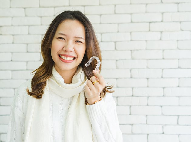 Woman in white sweater smiling holding Invisalign