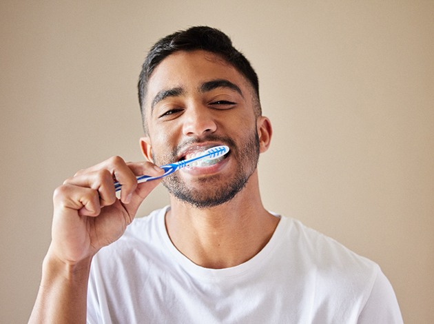 Man in white t-shirt brushing with blue and white standard toothbrush