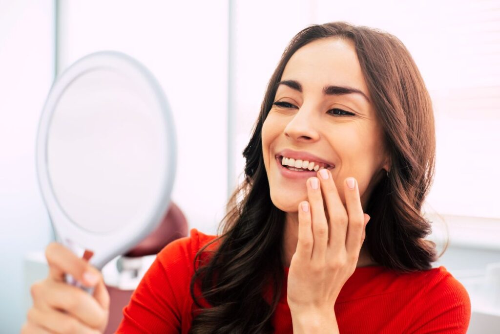 A woman smiling at her face in the mirror at the dentist’s office.